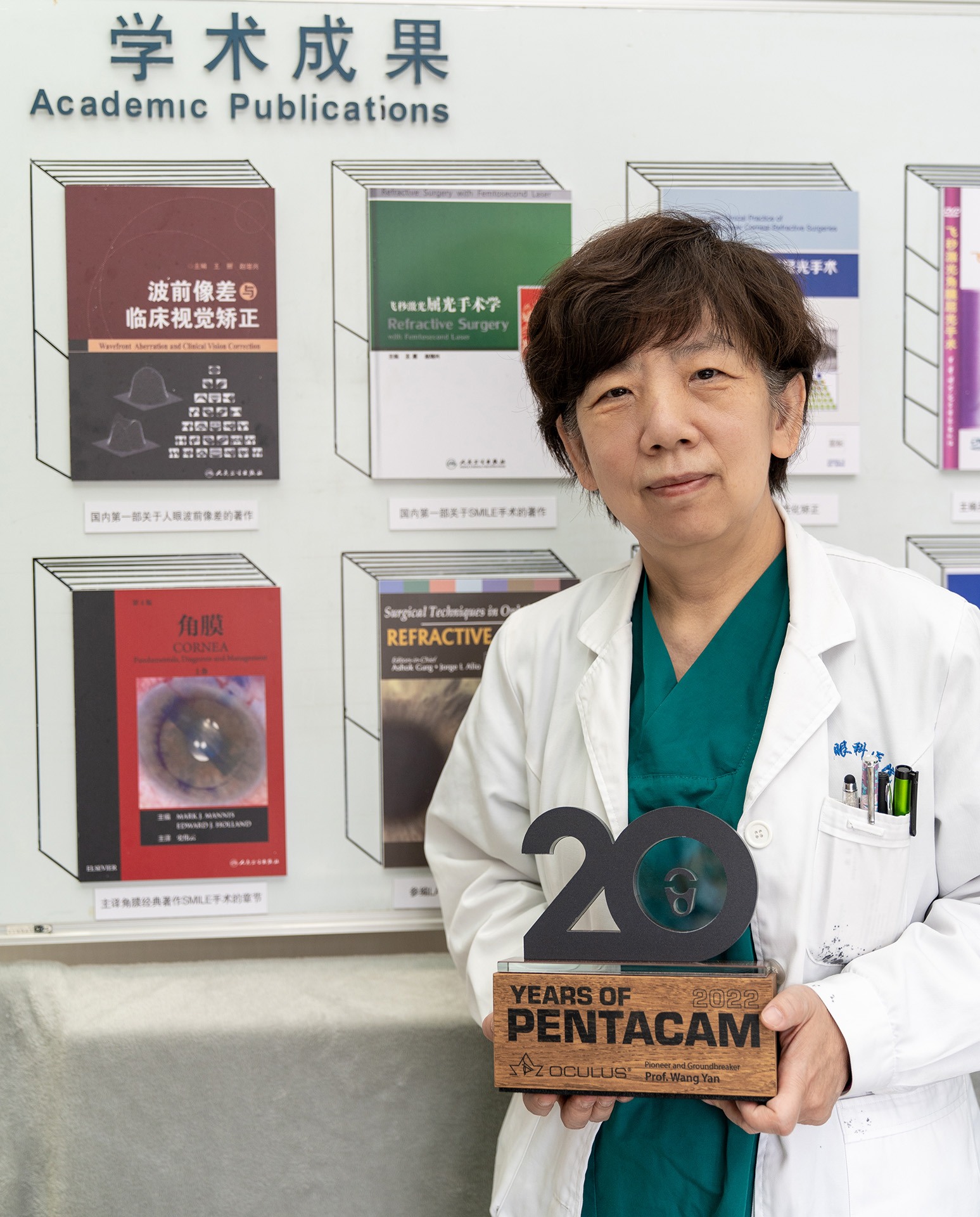 Prof Wang Yan holds her Pentacam® 20th Anniversary Trophy with some of their team's academic publications on the back wall