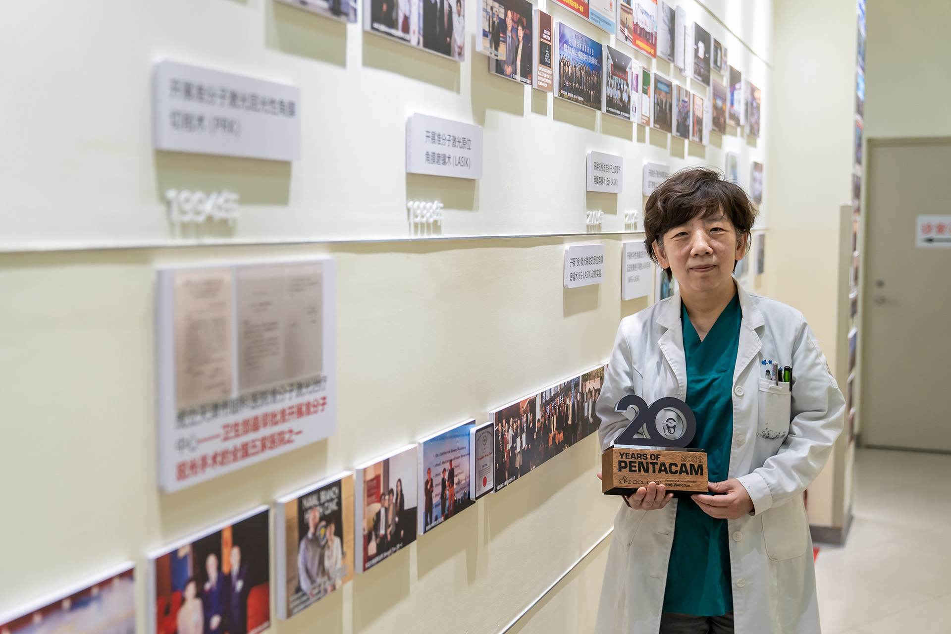Prof Wang Yan holds her Pentacam® 20th anniversary trophy, and the back wall shows the development of her refractive surgery laboratory for more than 20 years