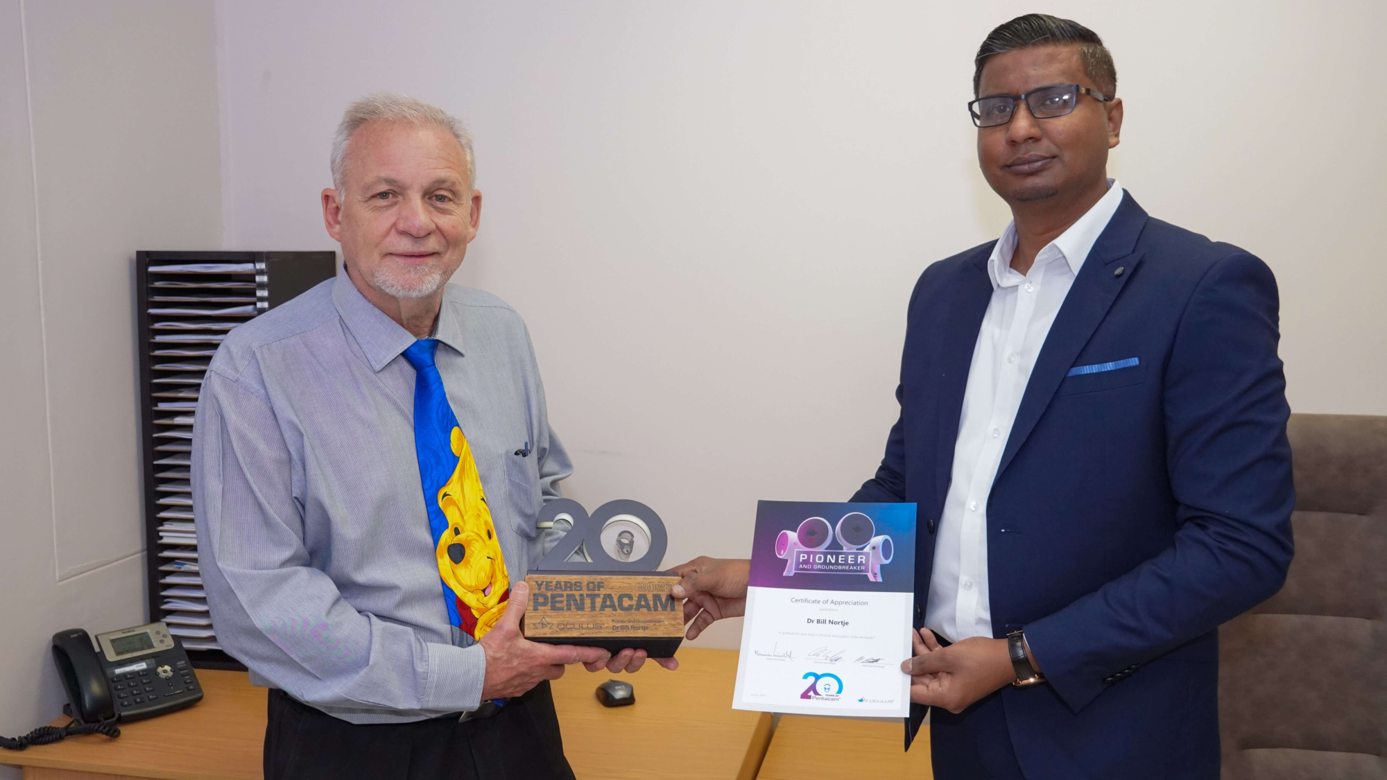 Dr Bill Nortje and Mr Neil Sivalingum, Senior Biomedical Engineer at Genop Healthcare (Pty) Ltd., holding the 20th Anniversary Pentacam® Trophy and Certificate of Appreciation.