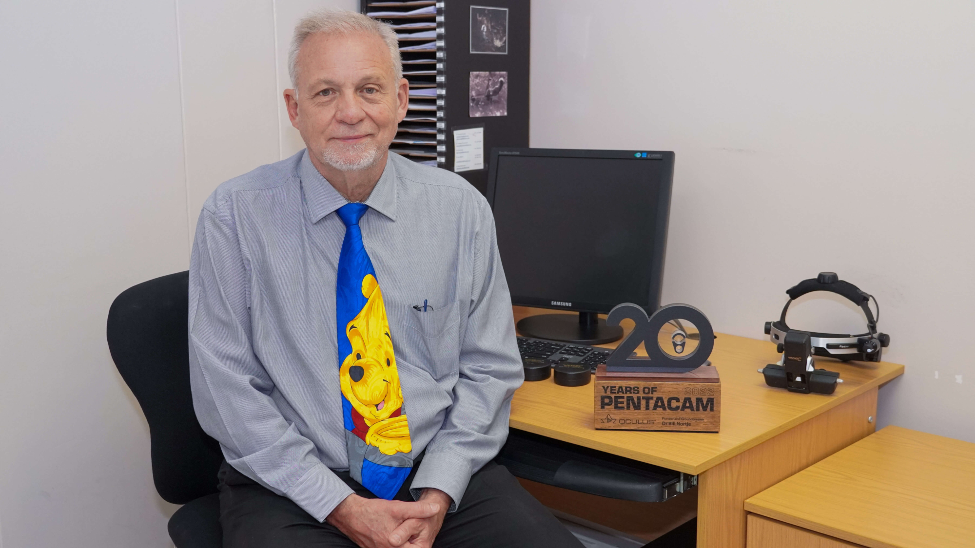 Dr Bill Nortje at his desk with the 20th Anniversary Pentacam® Trophy.